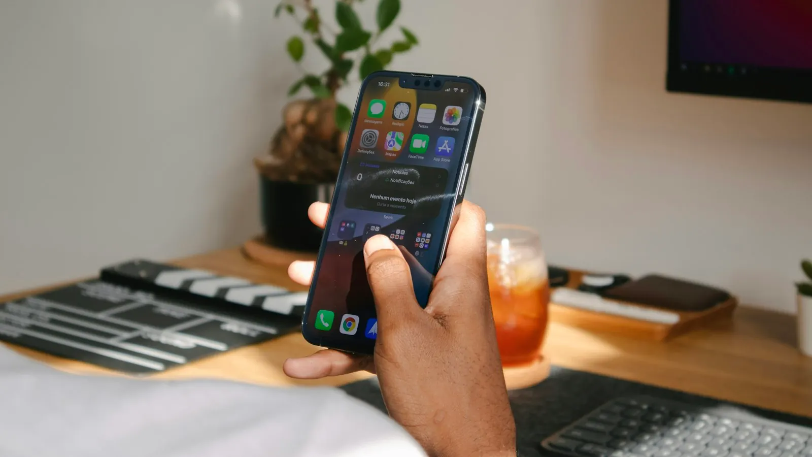 Hand holding a smartphone above a desk workspace