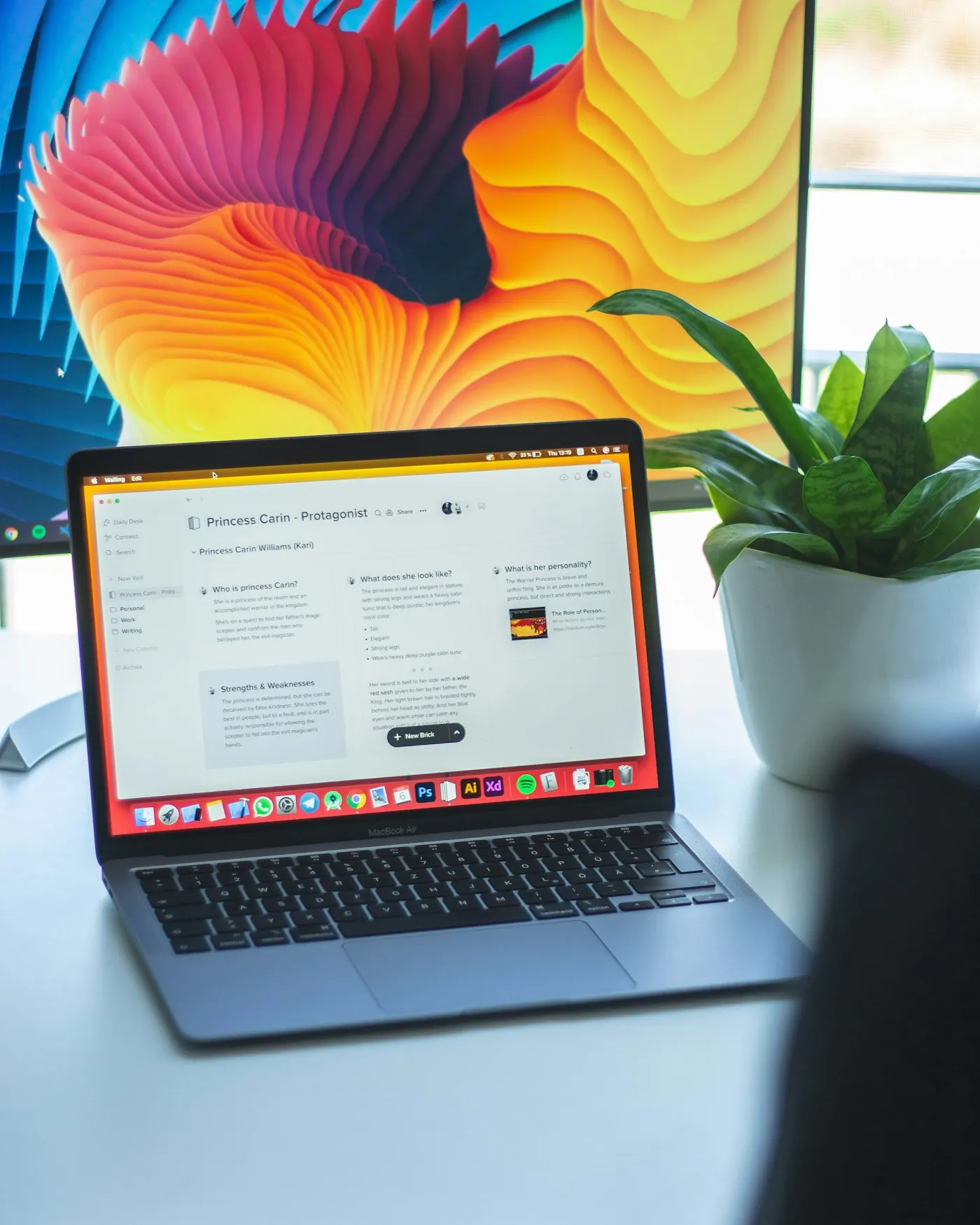 Laptop showing an organised workspace beside a monitor and plant